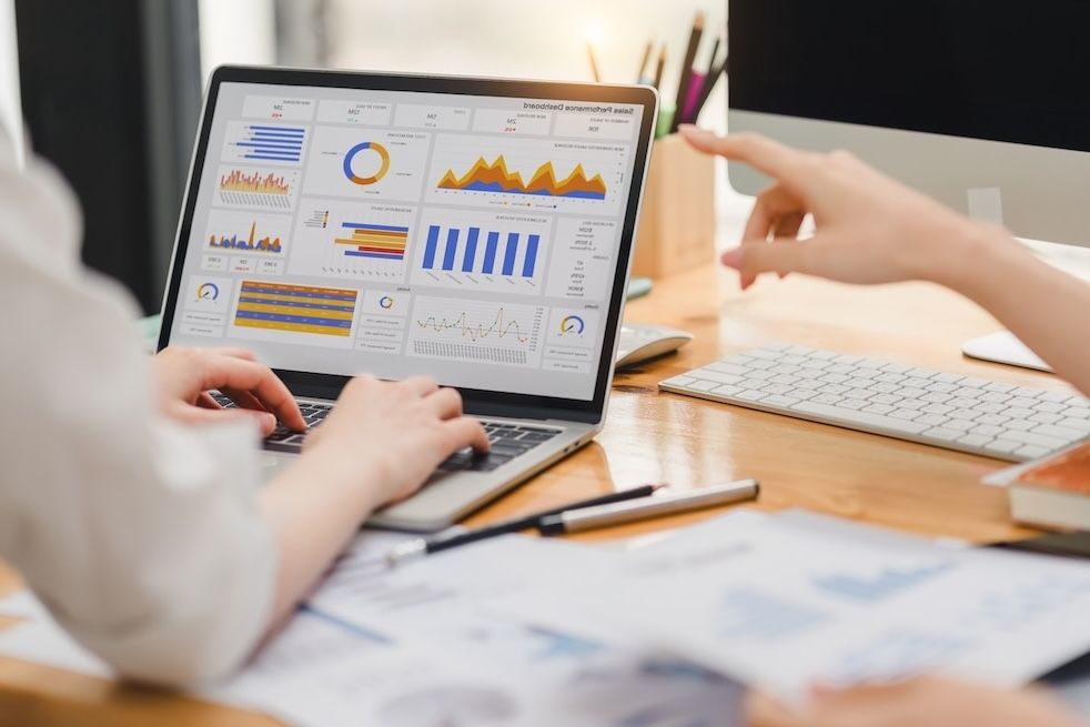 Close-up of two people analyzing a laptop screen displaying a sales performance dashboard with charts and graphs